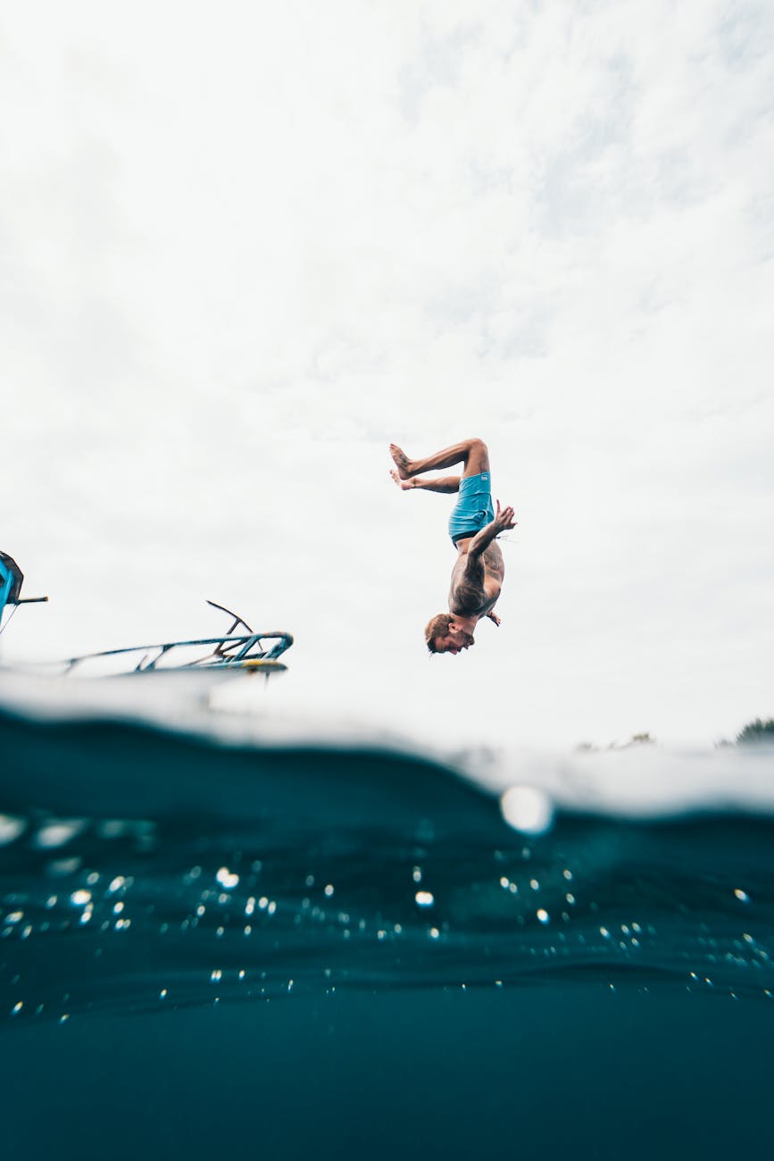 Man performing a backflip dive into the tropical ocean off a boat in Indonesia.