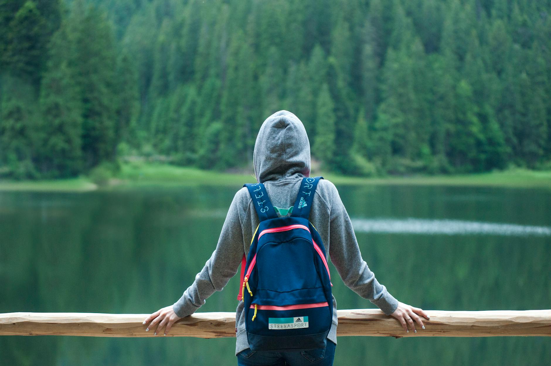 A person in a hoodie stands by a serene lake surrounded by lush greenery, enjoying the peaceful outdoors. A person in a hoodie stands by a serene lake surrounded by lush greenery, enjoying the peaceful outdoors.