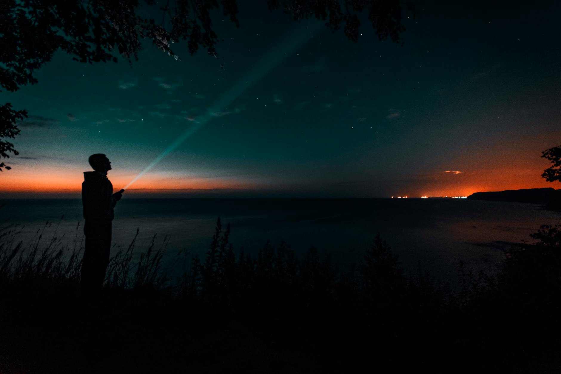Silhouette of a person with a flashlight by the sea under a starry sky during twilight. Silhouette of a person with a flashlight by the sea under a starry sky during twilight.