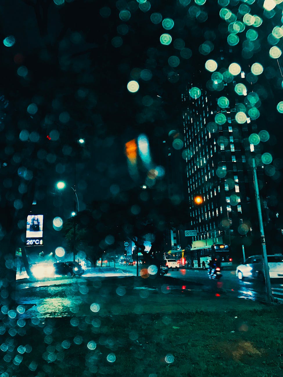 Dynamic urban night scene with illuminated skyscrapers and raindrops on window.