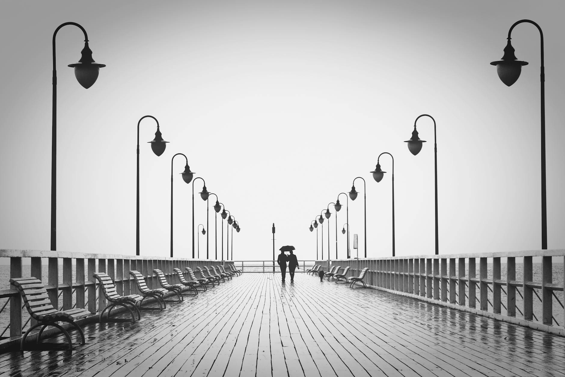 A couple holding umbrellas walks on a rainy boardwalk, embodying romance and tranquility. A couple holding umbrellas walks on a rainy boardwalk, embodying romance and tranquility.