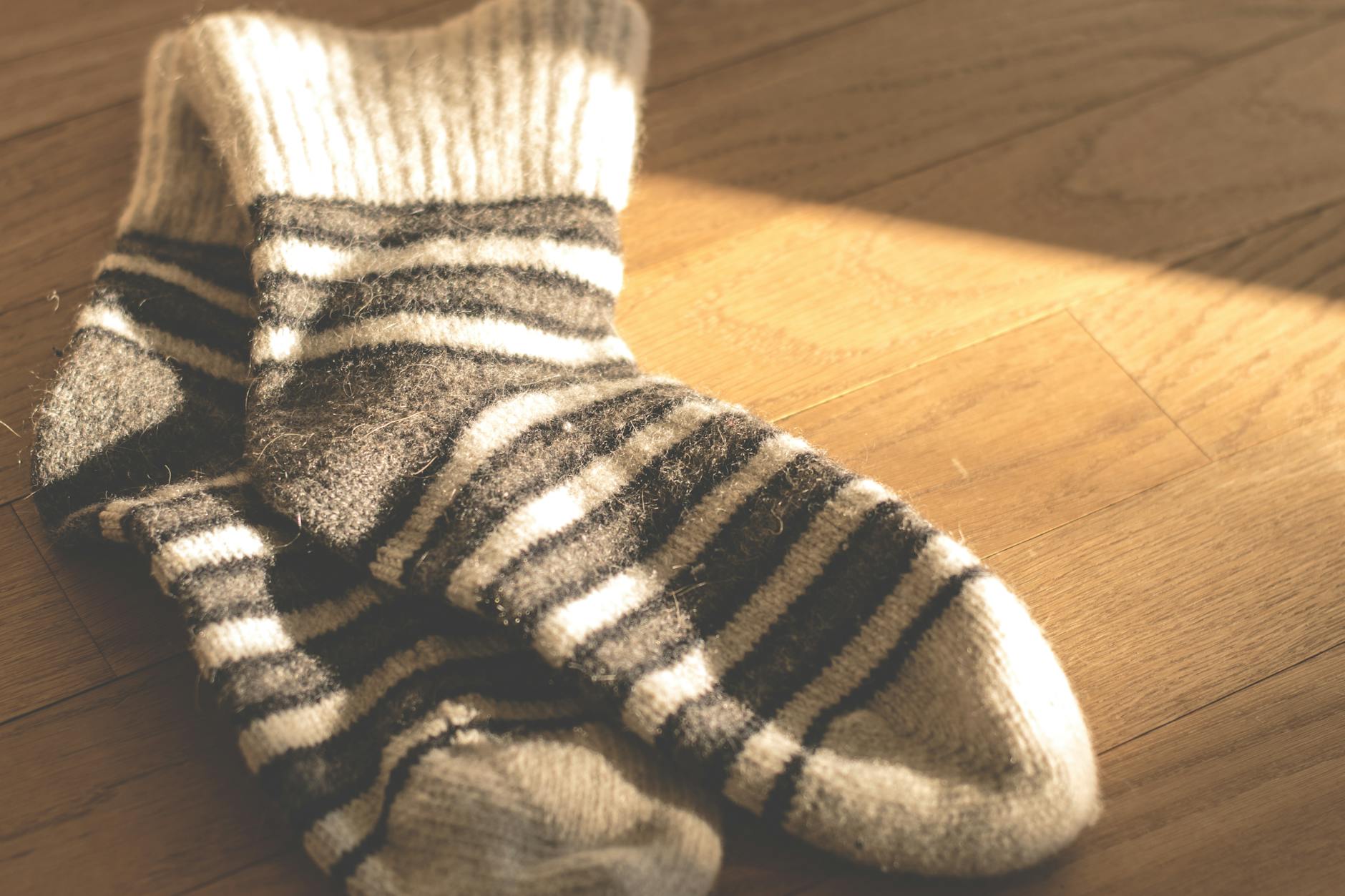 Warm knitted striped socks on a sunlit wooden floor, offering a cozy and stylish winter vibe. Warm knitted striped socks on a sunlit wooden floor, offering a cozy and stylish winter vibe.