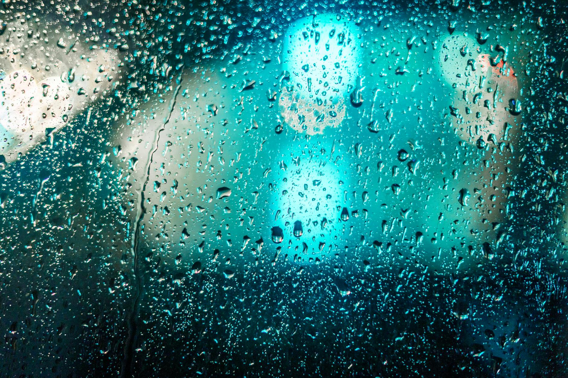 Raindrops on glass with blurred colorful lights creating a moody abstract background. Raindrops on glass with blurred colorful lights creating a moody abstract background.