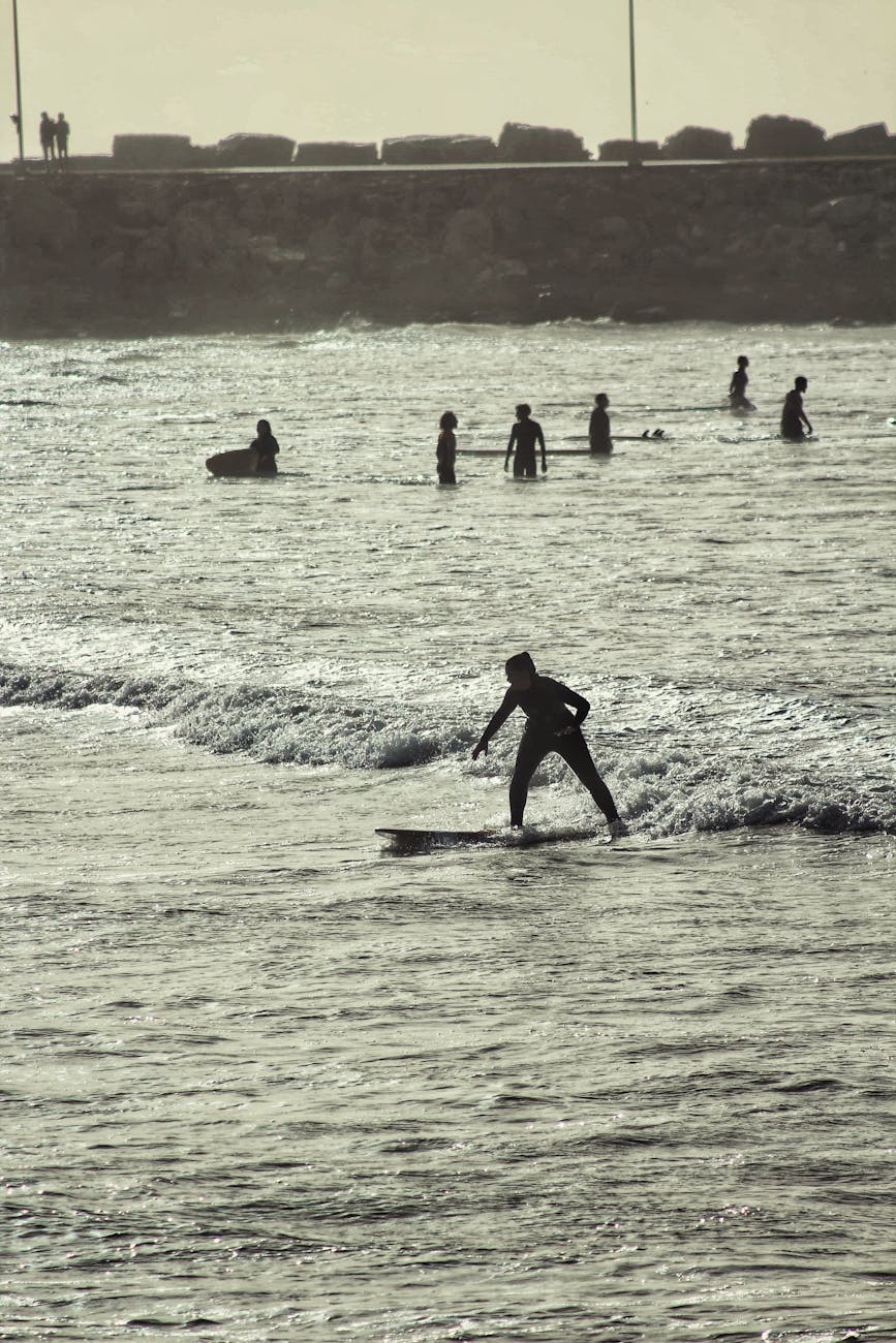 A surfer catching a wave at sunset with silhouettes of people in the background.