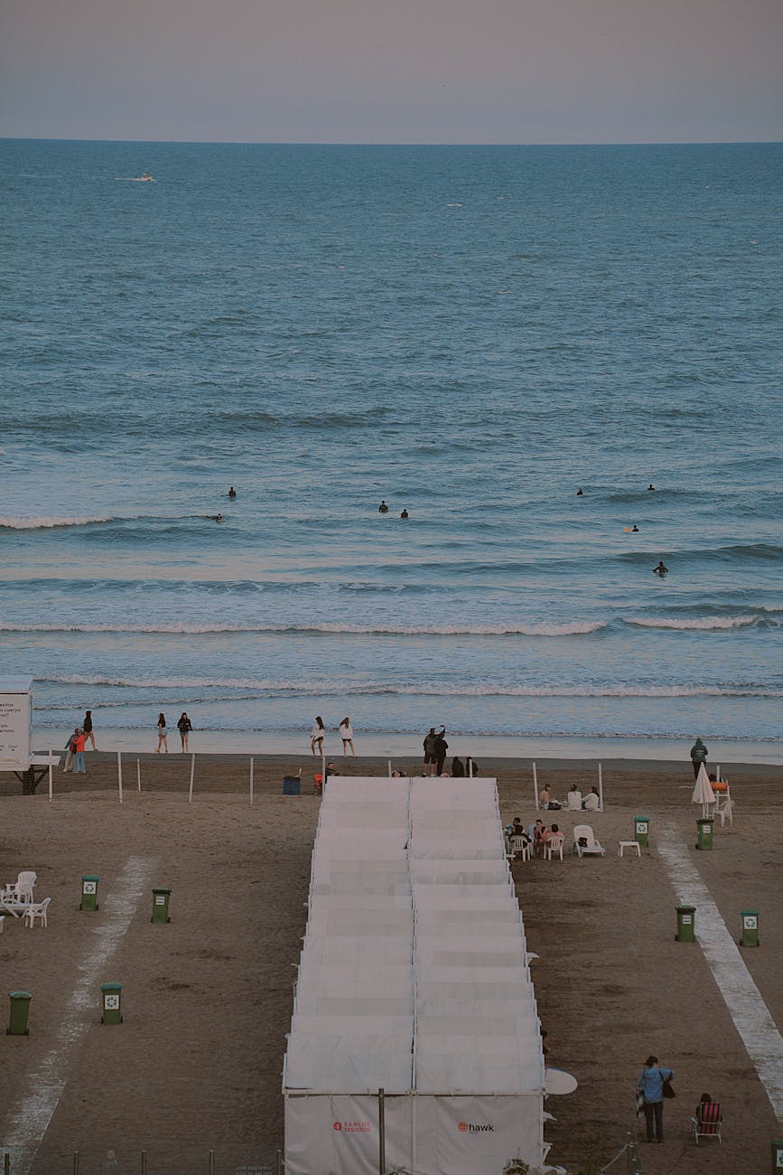 A serene beach scene featuring white tents, people walking, and ocean waves crashing on the shore.