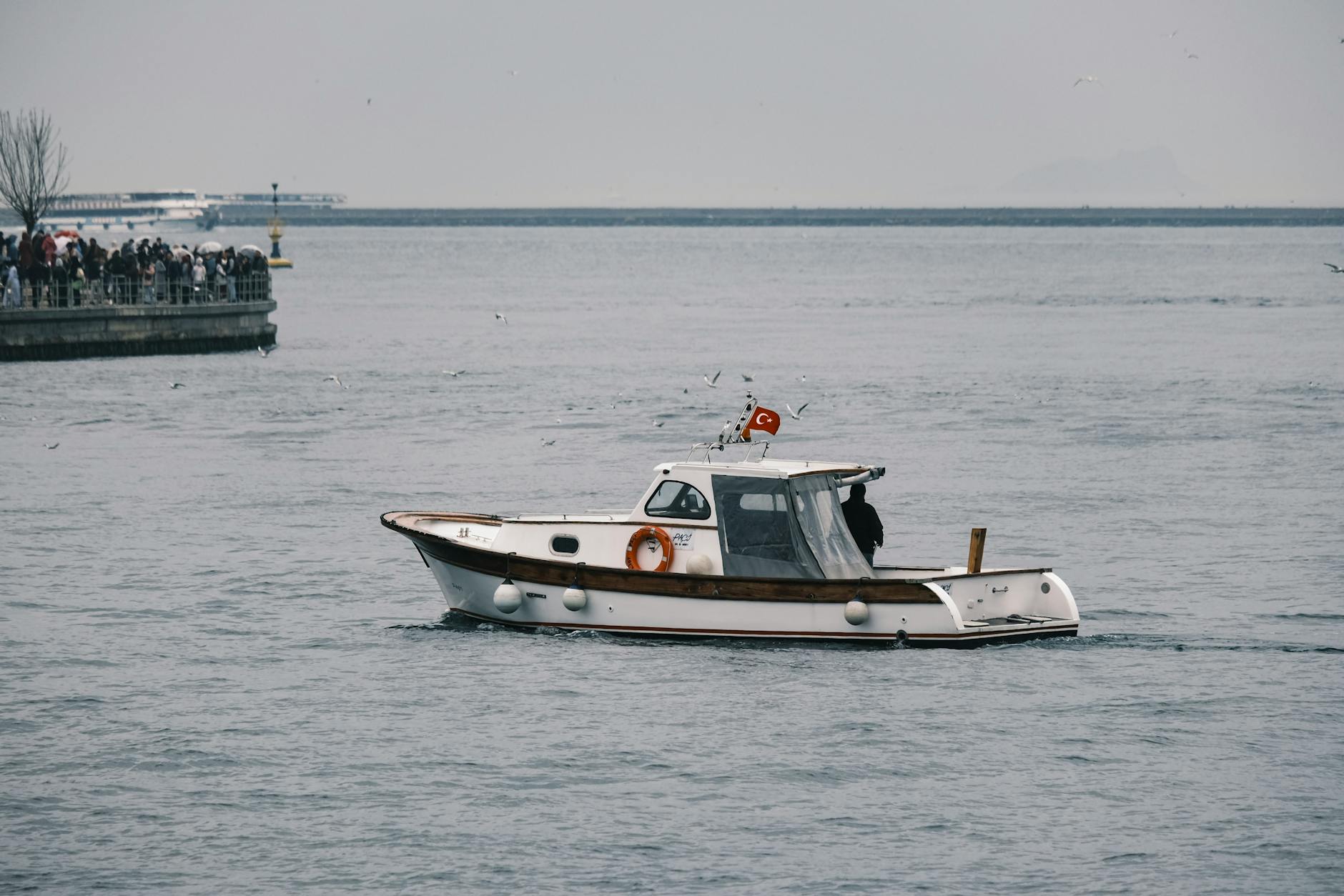 A small boat sails on the Bosphorus with a view of İstanbul and a crowd nearby. A small boat sails on the Bosphorus with a view of İstanbul and a crowd nearby.