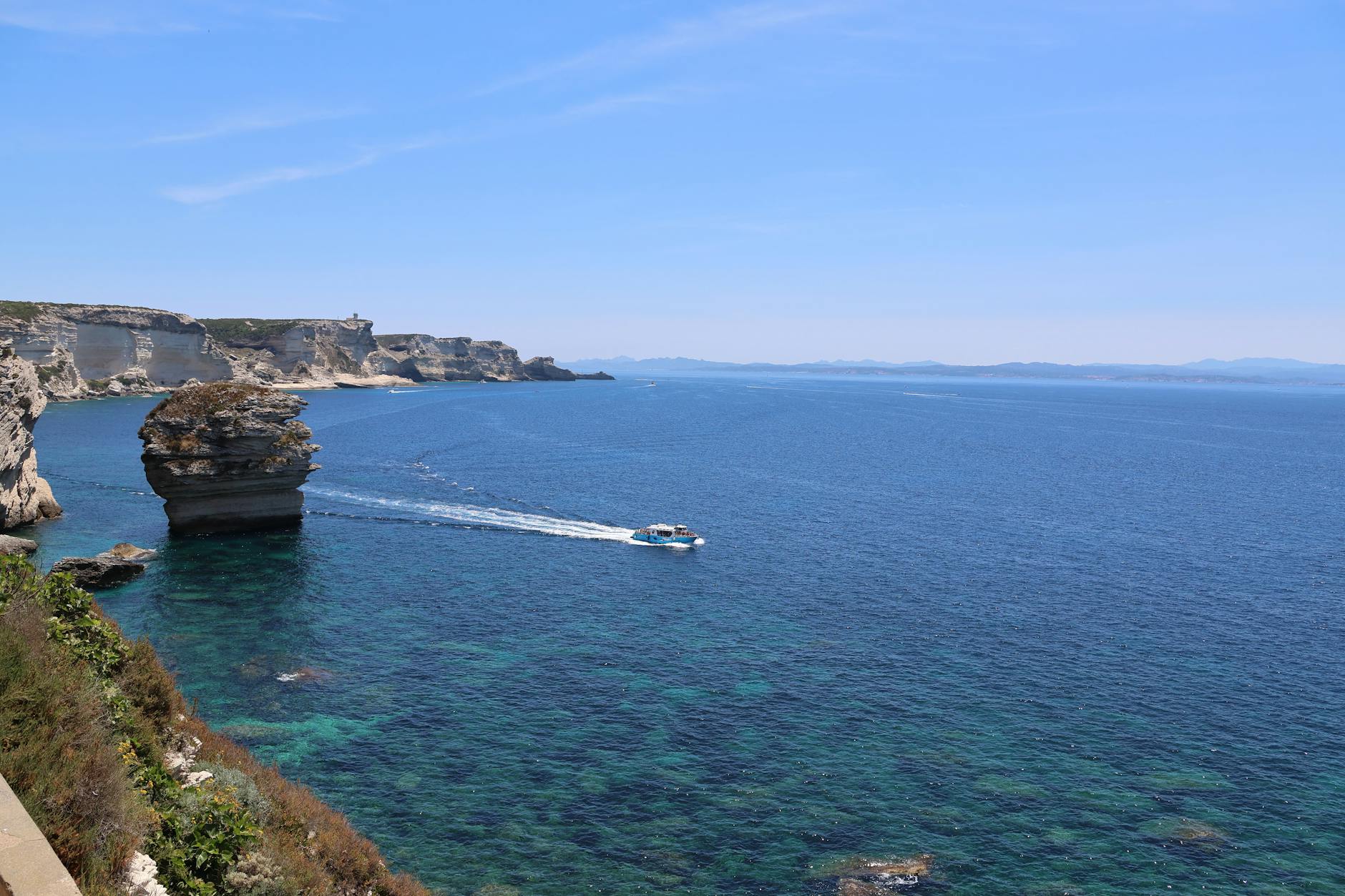 Scenic view of Bonifacio’s limestone cliffs with a boat gliding through the azure Mediterranean waters. Scenic view of Bonifacio’s limestone cliffs with a boat gliding through the azure Mediterranean waters.