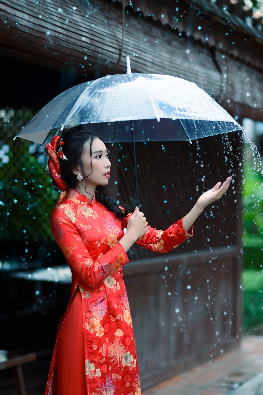 A young woman in red ao dai holds an umbrella during a rain shower. A young woman in red ao dai holds an umbrella during a rain shower.