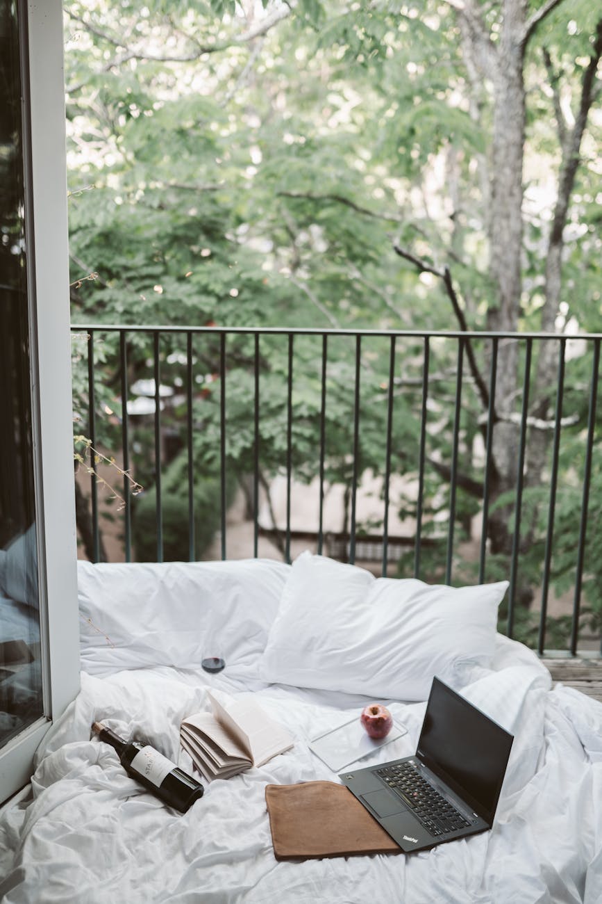 Relaxing on a cozy balcony with a laptop and wine bottle, surrounded by lush greenery. Relaxing on a cozy balcony with a laptop and wine bottle, surrounded by lush greenery.