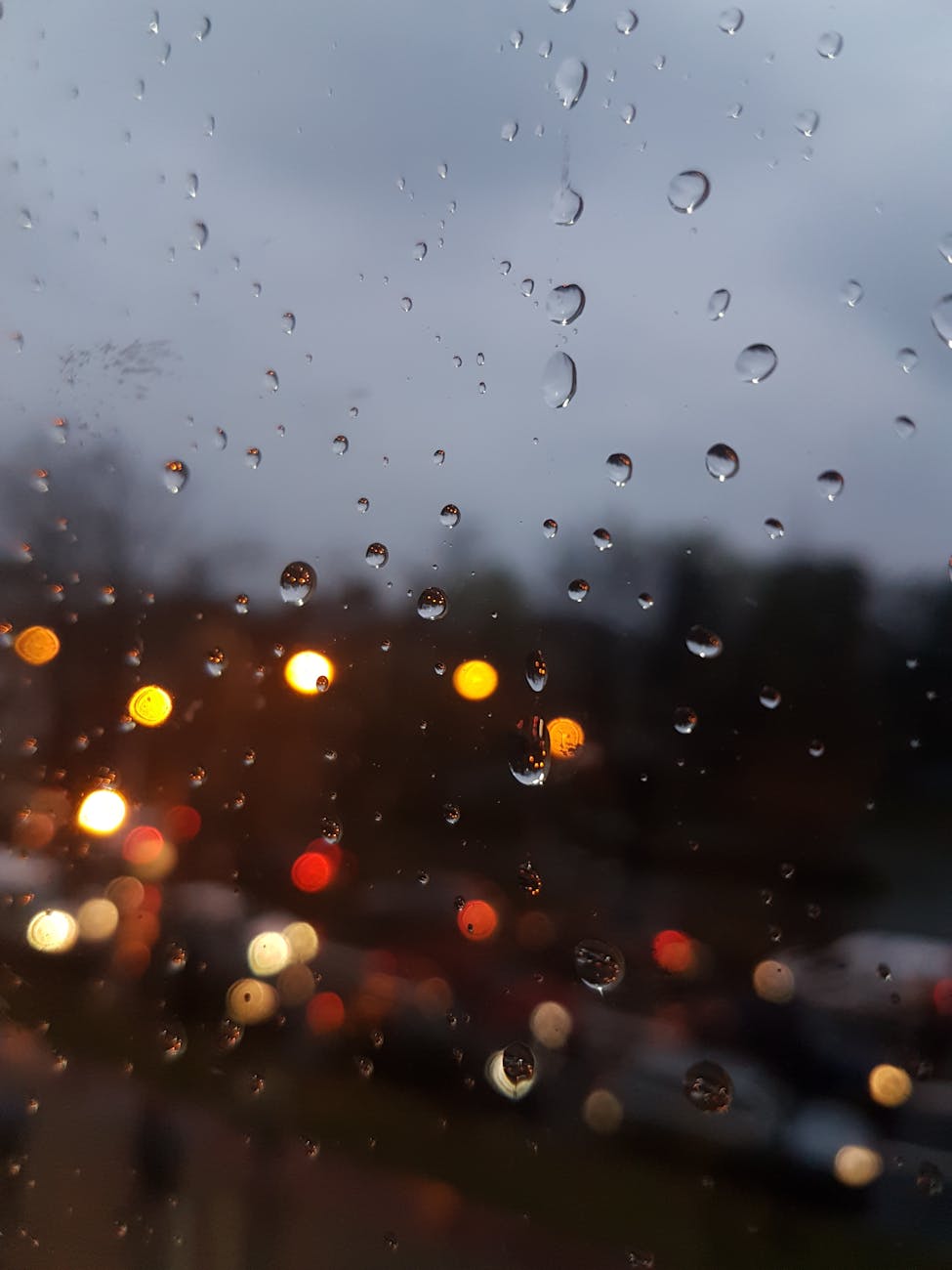 Raindrops on a window with blurred city lights creating a bokeh effect at twilight. Raindrops on a window with blurred city lights creating a bokeh effect at twilight.