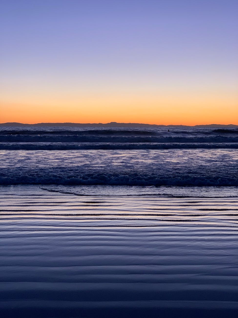 Beautiful sunset over the ocean with gentle waves and vibrant sky colors.