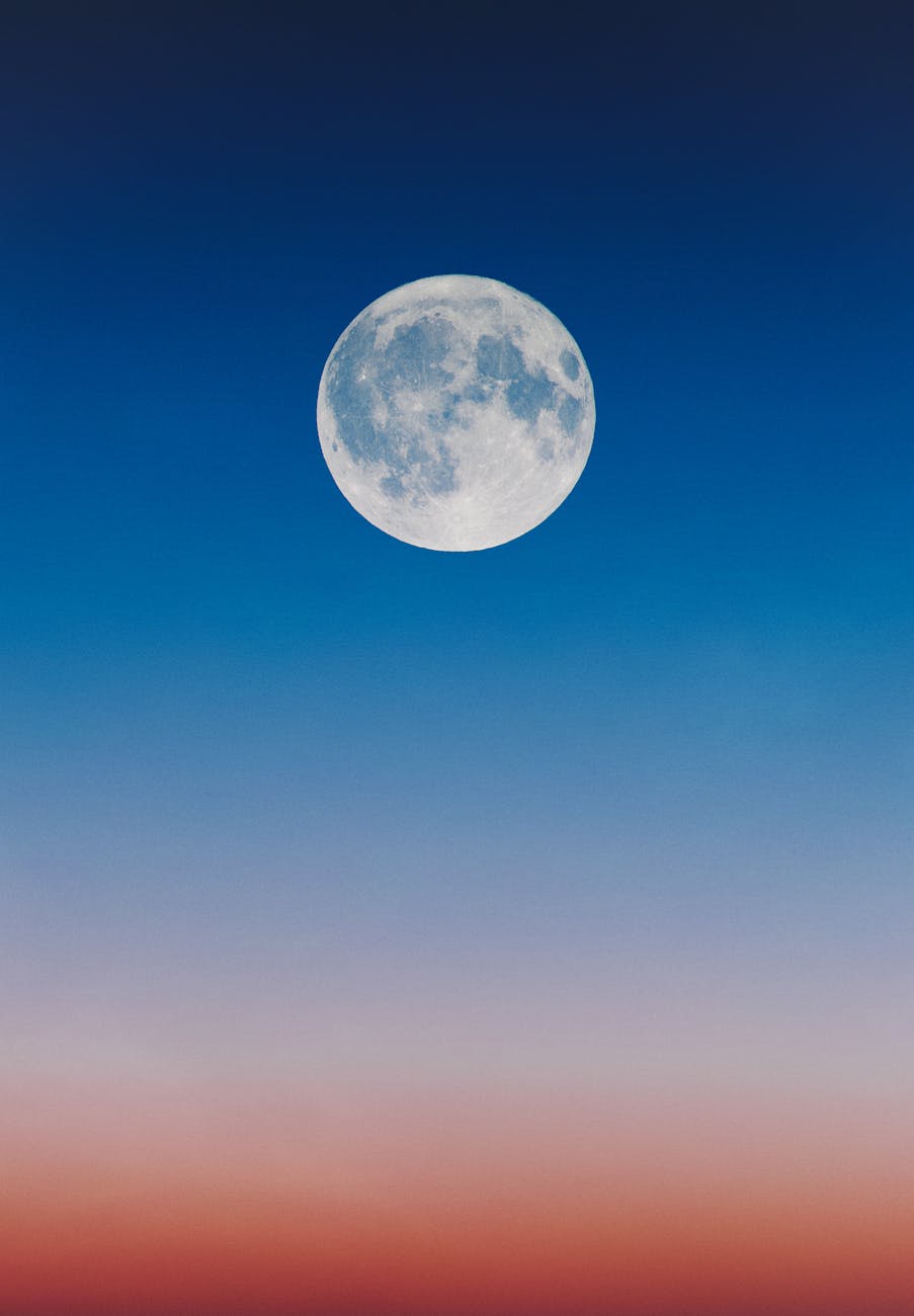 A serene full moon set against a gradient twilight sky, blending hues of blue and orange. A serene full moon set against a gradient twilight sky, blending hues of blue and orange.