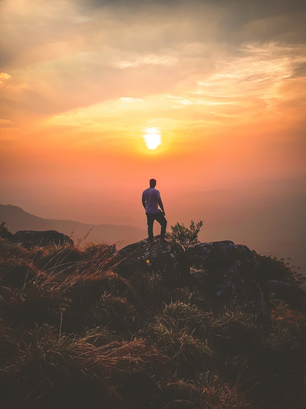 A lone hiker admires a stunning sunset view from Ponmudi Peak, creating a serene landscape scene. A lone hiker admires a stunning sunset view from Ponmudi Peak, creating a serene landscape scene.