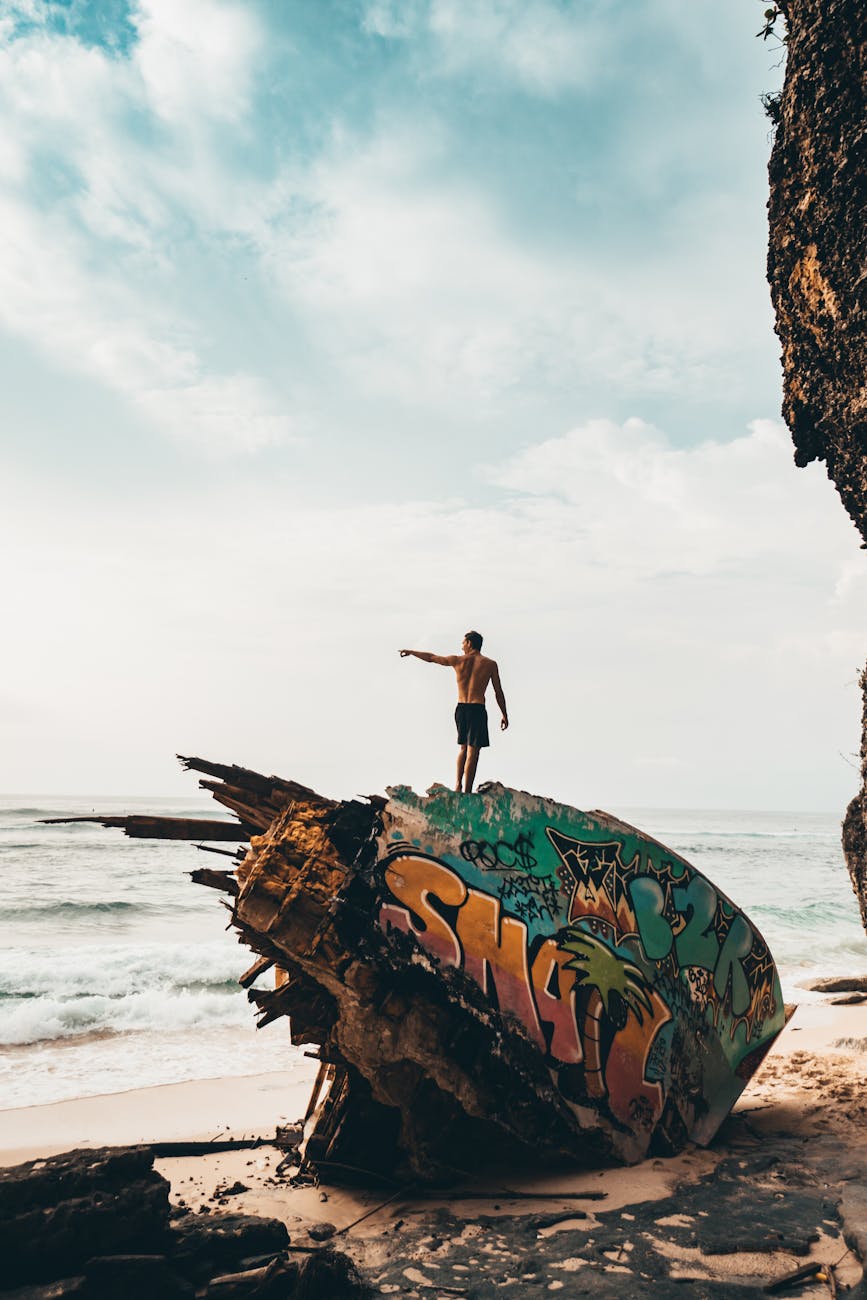 A man stands atop a graffiti-painted shipwreck on a beach in Bali, Indonesia, capturing moments of adventure and exploration. A man stands atop a graffiti-painted shipwreck on a beach in Bali, Indonesia, capturing moments of adventure and exploration.