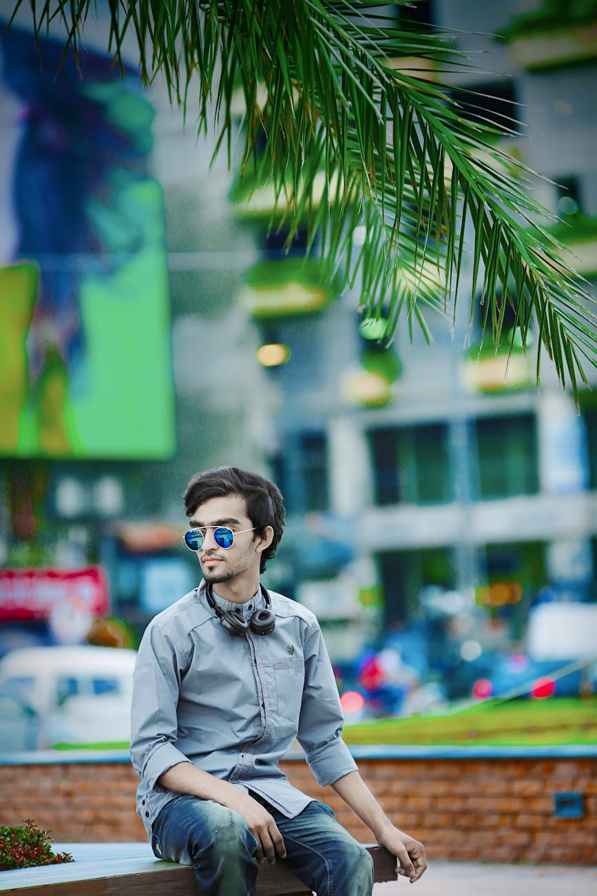 Stylish young man sitting in a vibrant urban park, wearing sunglasses and headphones. Stylish young man sitting in a vibrant urban park, wearing sunglasses and headphones.