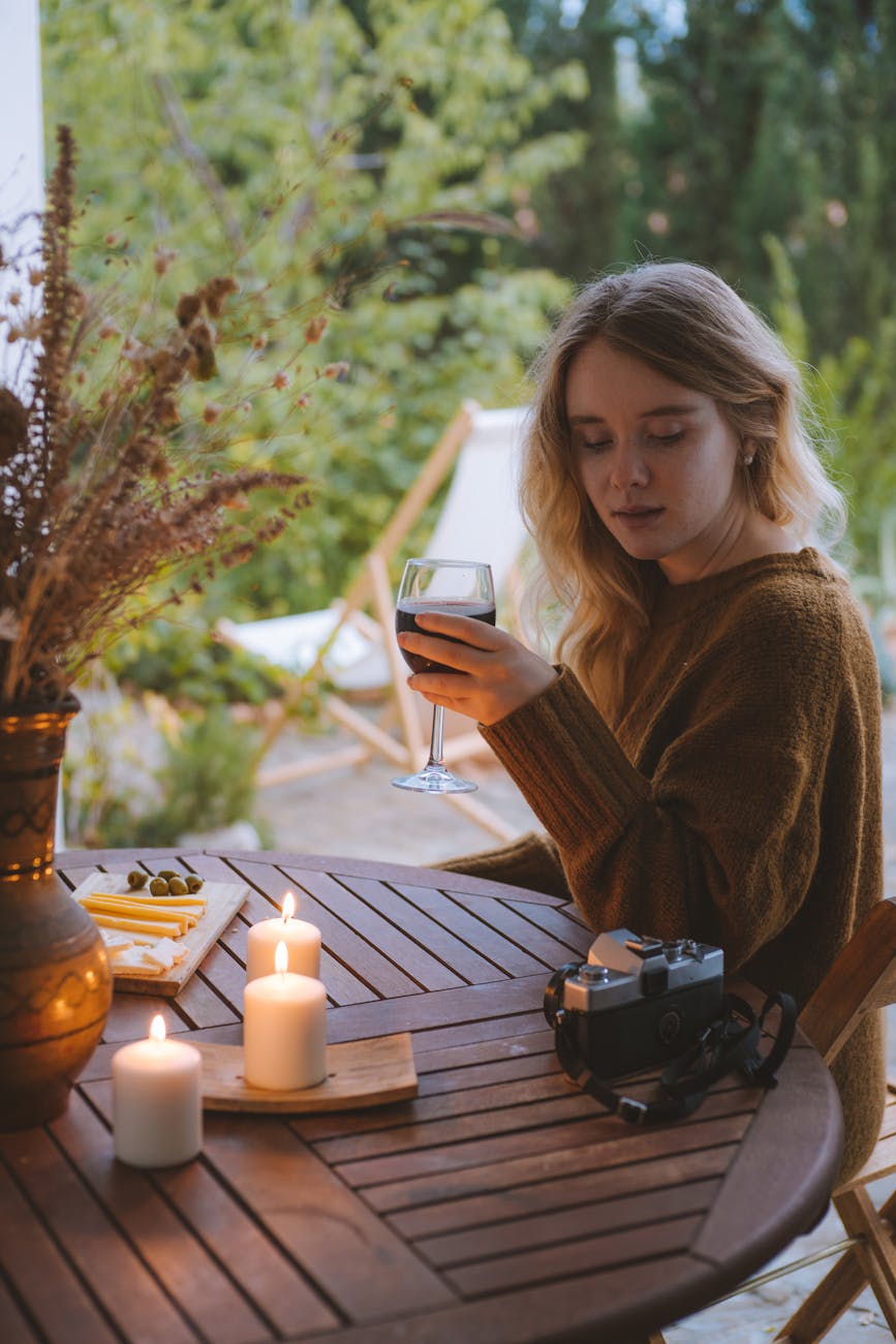 A young woman enjoys a peaceful moment with wine, surrounded by candles on an outdoor patio. A young woman enjoys a peaceful moment with wine, surrounded by candles on an outdoor patio.