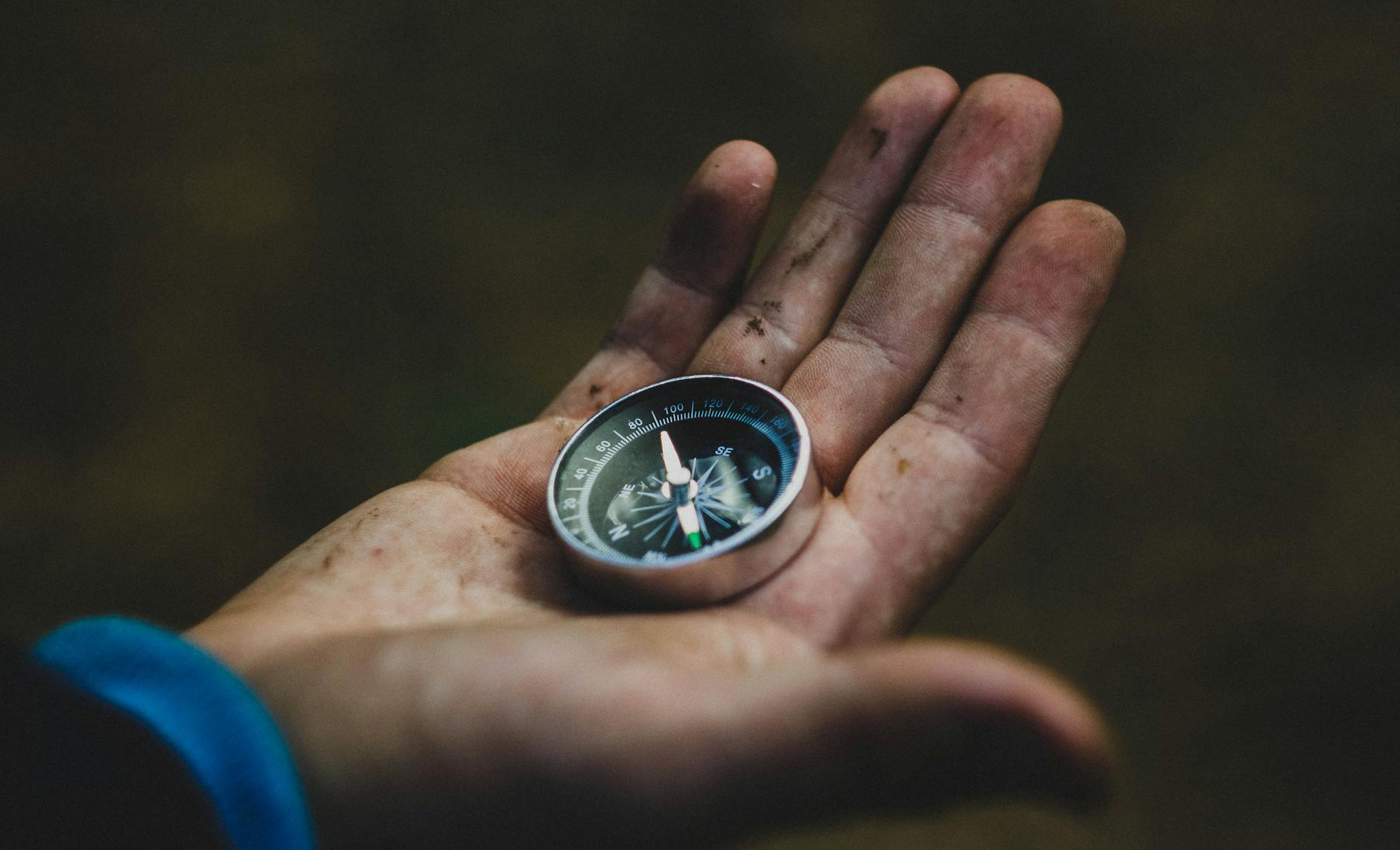 A close-up of a compass held in a dirty hand, symbolizing adventure and navigation. A close-up of a compass held in a dirty hand, symbolizing adventure and navigation.