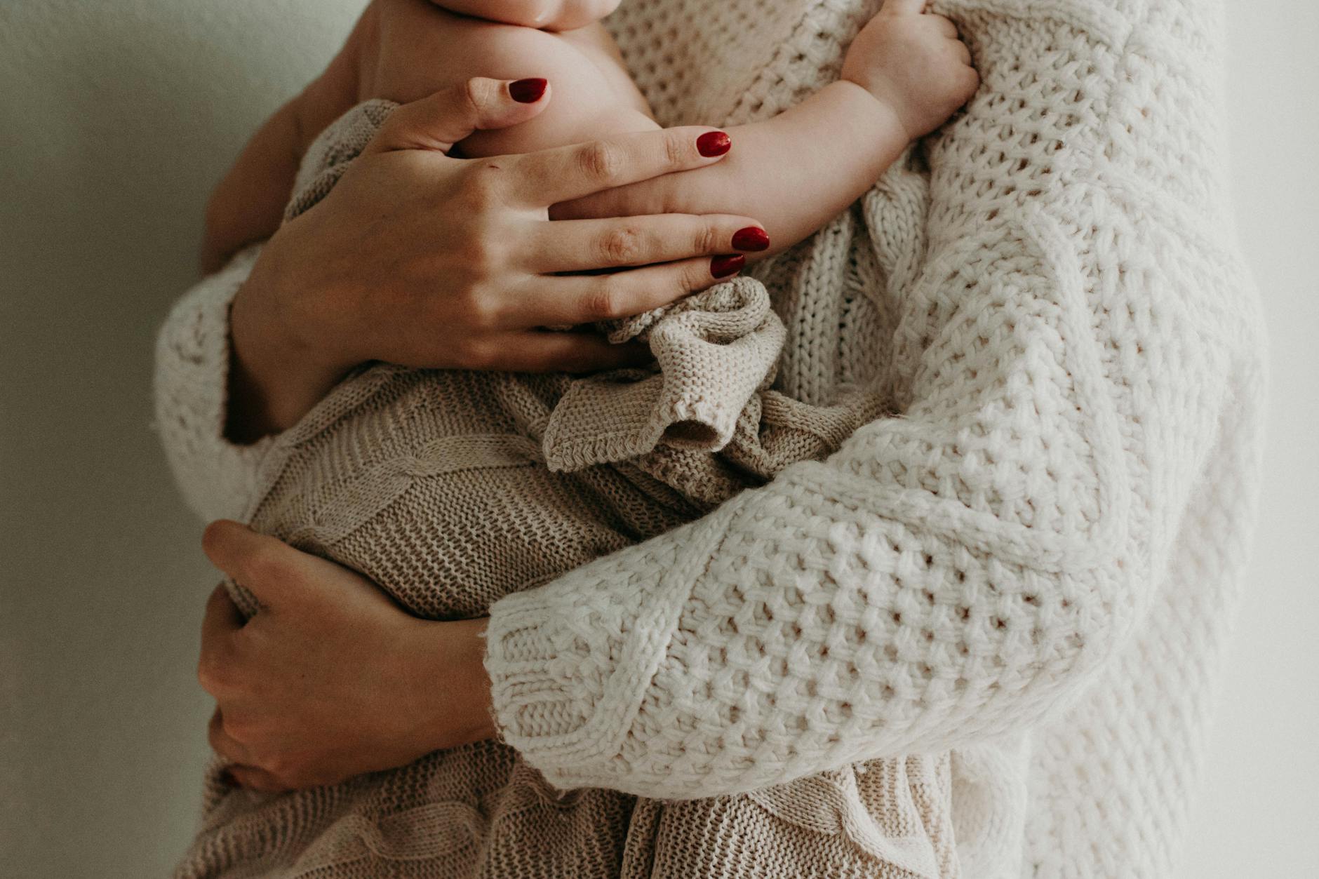Close-up of a mother holding her baby in warm knitwear, conveying love and togetherness. Close-up of a mother holding her baby in warm knitwear, conveying love and togetherness.