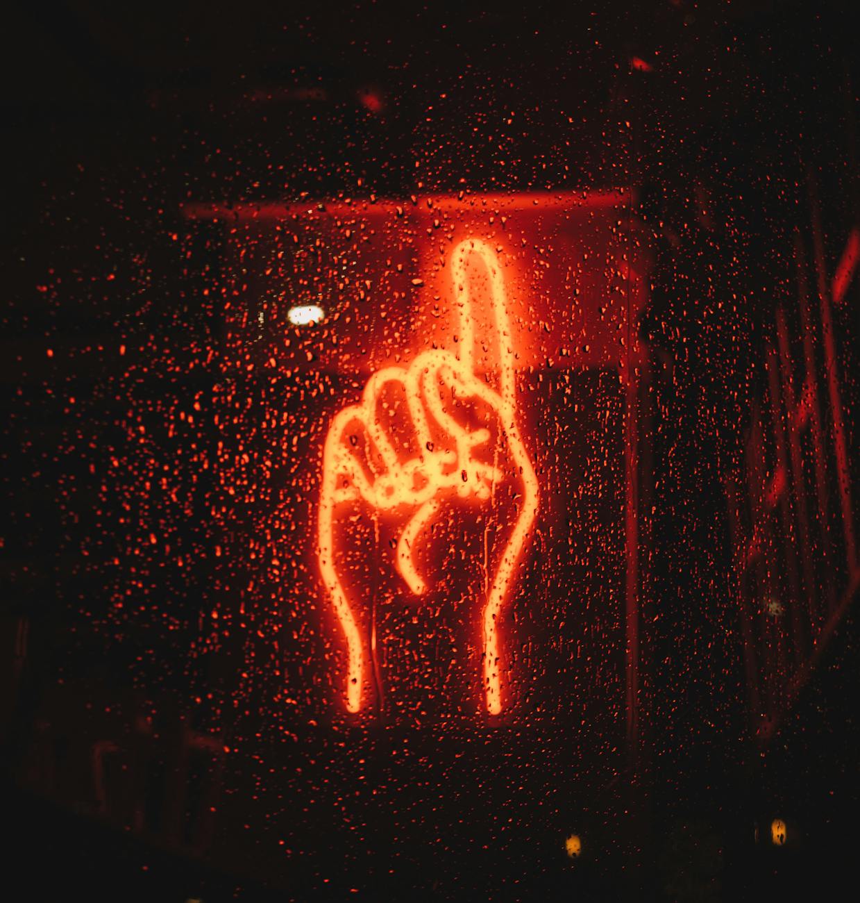 A vibrant neon hand sign seen through a wet window, creating a dramatic urban night scene. A vibrant neon hand sign seen through a wet window, creating a dramatic urban night scene.