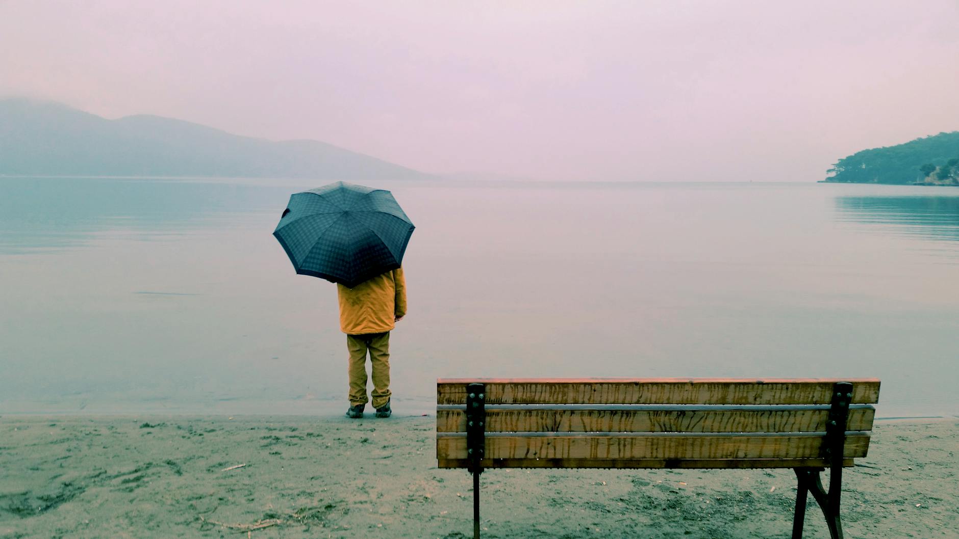 A person holding an umbrella stands alone by a peaceful lake, evoking calm and reflection. A person holding an umbrella stands alone by a peaceful lake, evoking calm and reflection.
