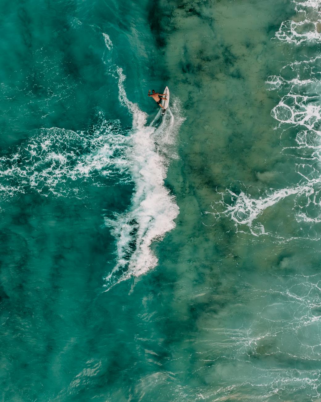 Top view of a surfer in turquoise Greek waters, capturing the thrill of surfing.