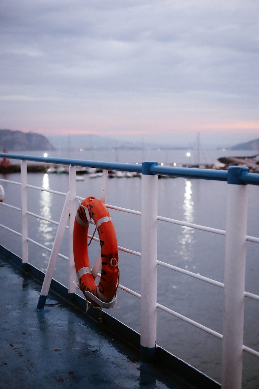 Ferry railing with lifebuoy overlooking serene harbor at dusk. Calm and peaceful ambiance.