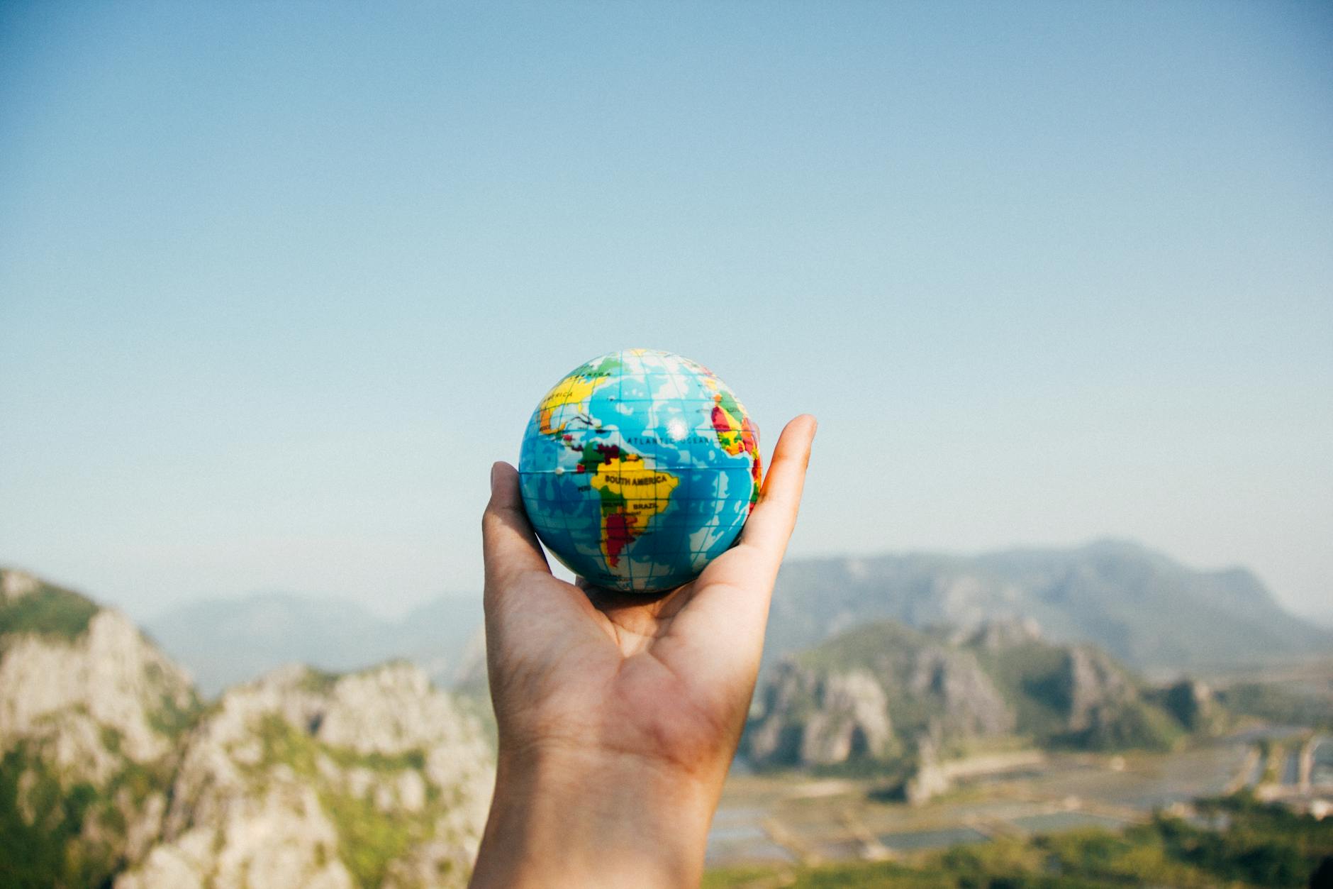 Hand holding a globe against a mountain background symbolizing travel and exploration. Hand holding a globe against a mountain background symbolizing travel and exploration.