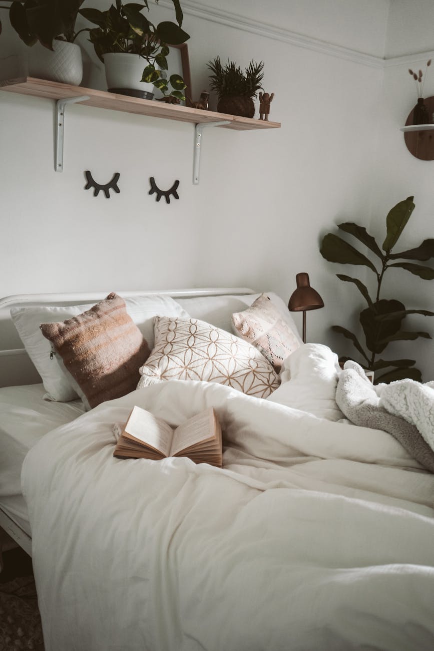 Warm and inviting bedroom setup with decorative pillows, plants, and an open book for a cozy ambiance. Warm and inviting bedroom setup with decorative pillows, plants, and an open book for a cozy ambiance.