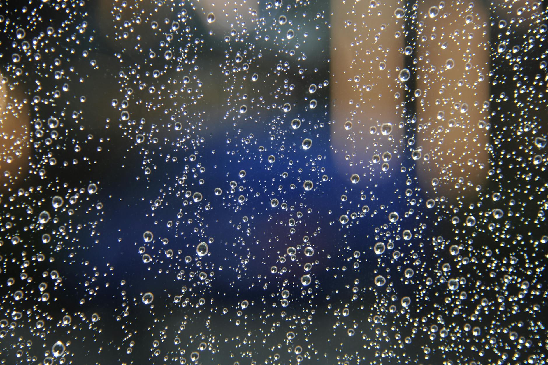 Macro shot capturing raindrops on glass with a blurred background. Macro shot capturing raindrops on glass with a blurred background.