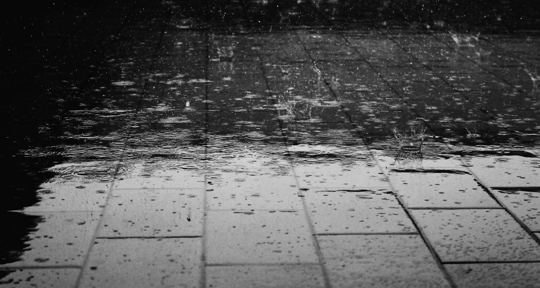Monochrome image of raindrops creating splashes on a wet paved surface. Monochrome image of raindrops creating splashes on a wet paved surface.