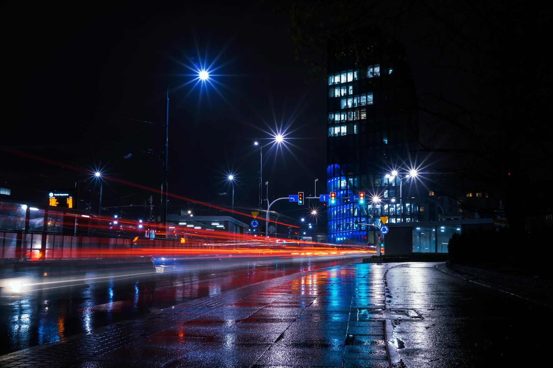 Illuminated city street at night with vibrant light trails and urban skyline.