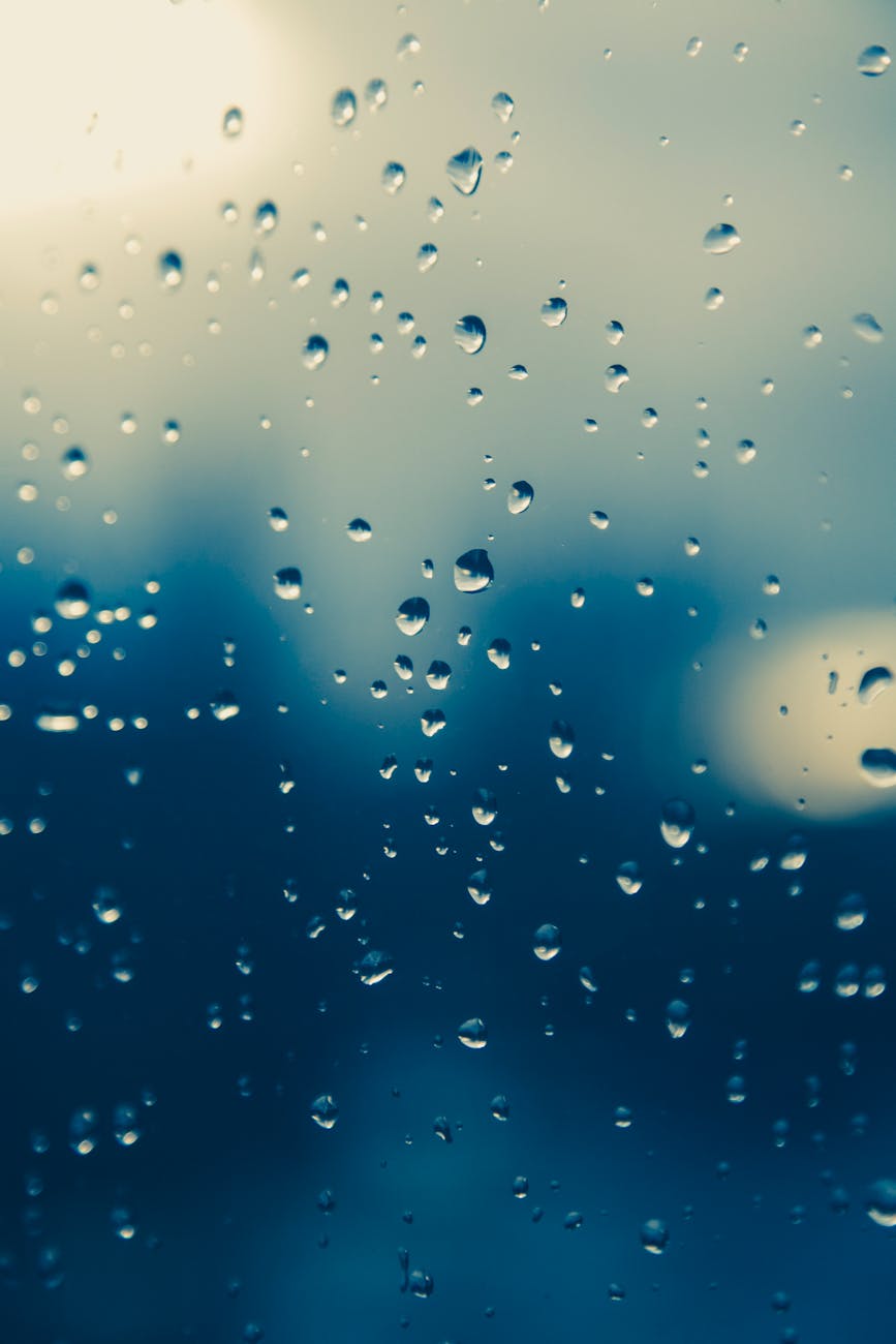 Close-up of raindrops on a window, creating a moody, blurred view outside.