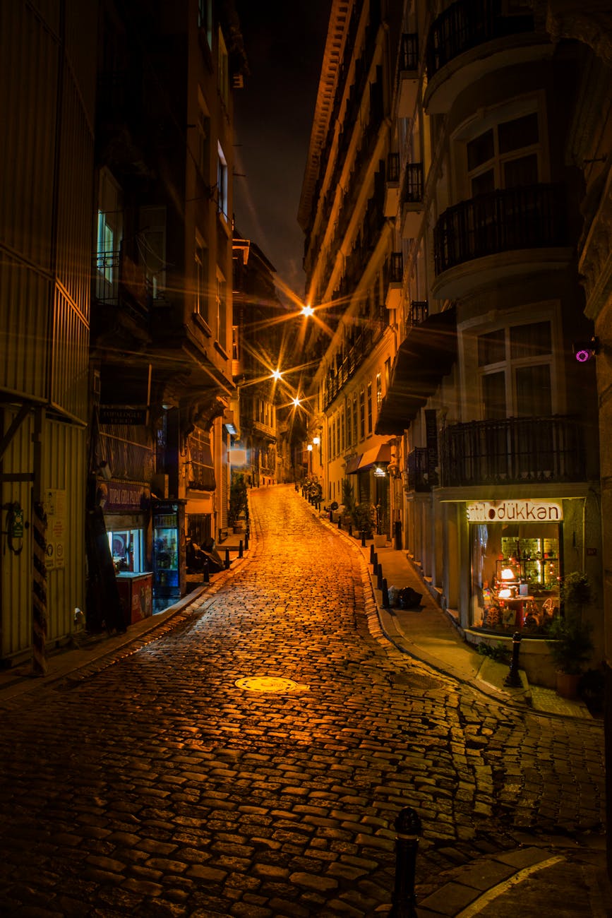 Illuminated cobblestone street in a lively urban area at night.