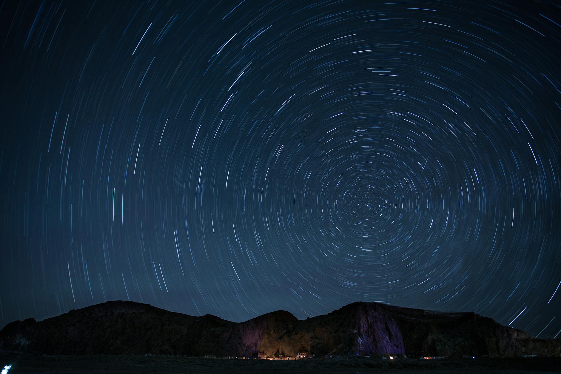A mesmerizing night sky showcasing rotating star trails over a mountainous landscape.