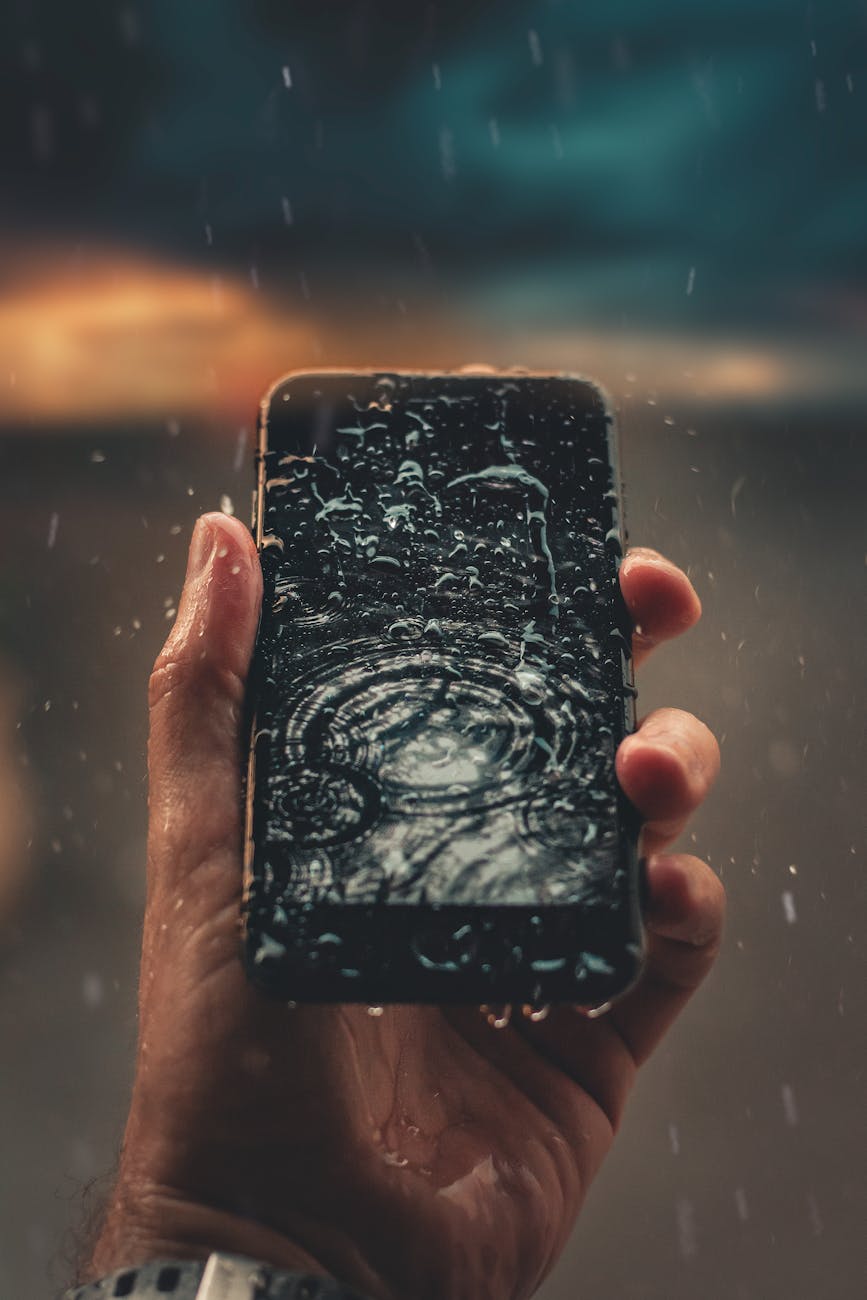 A person holds a smartphone with raindrops on screen, emphasizing water resistance. A person holds a smartphone with raindrops on screen, emphasizing water resistance.