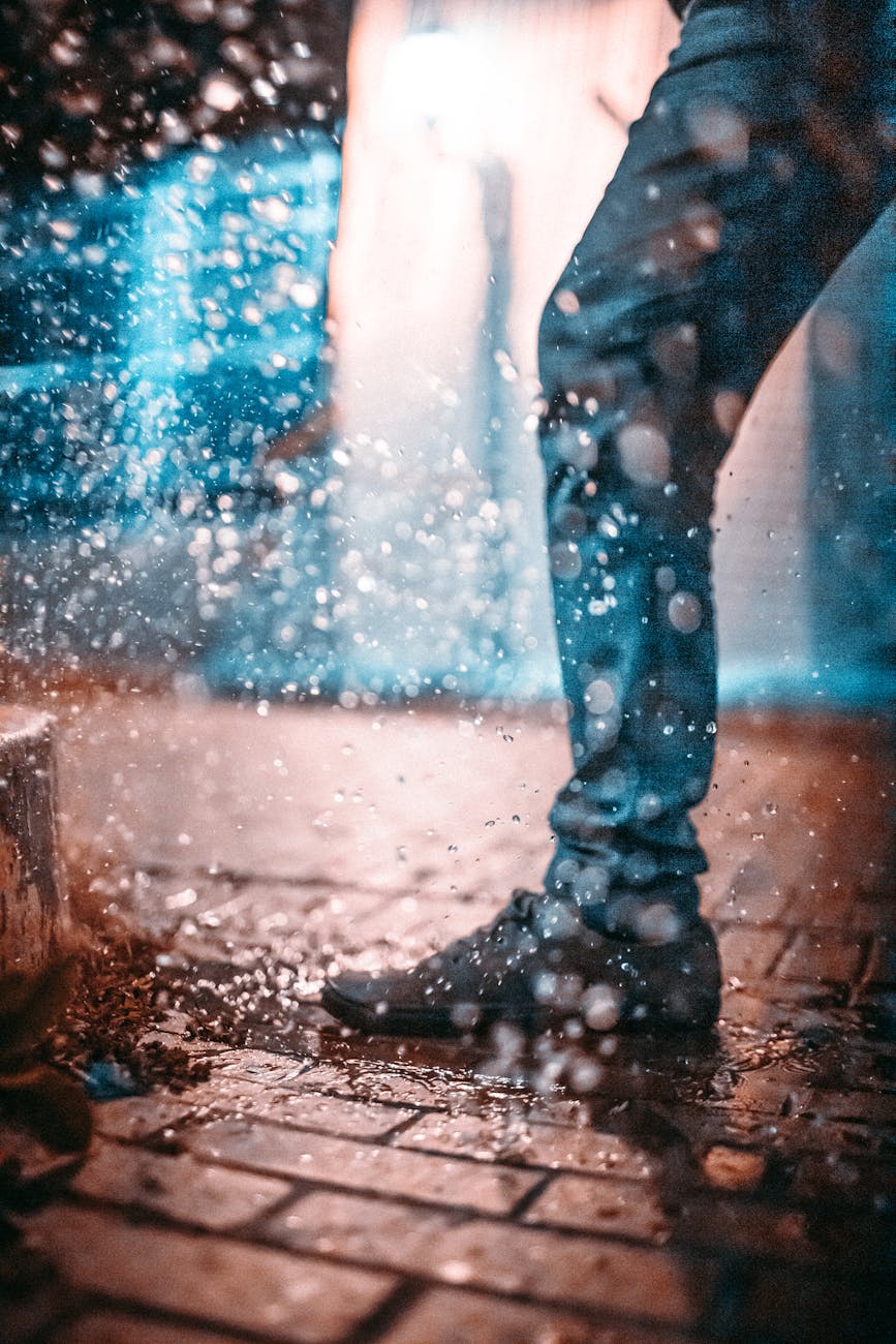 A stylish individual walks through a rainy urban street, creating dynamic water splashes.