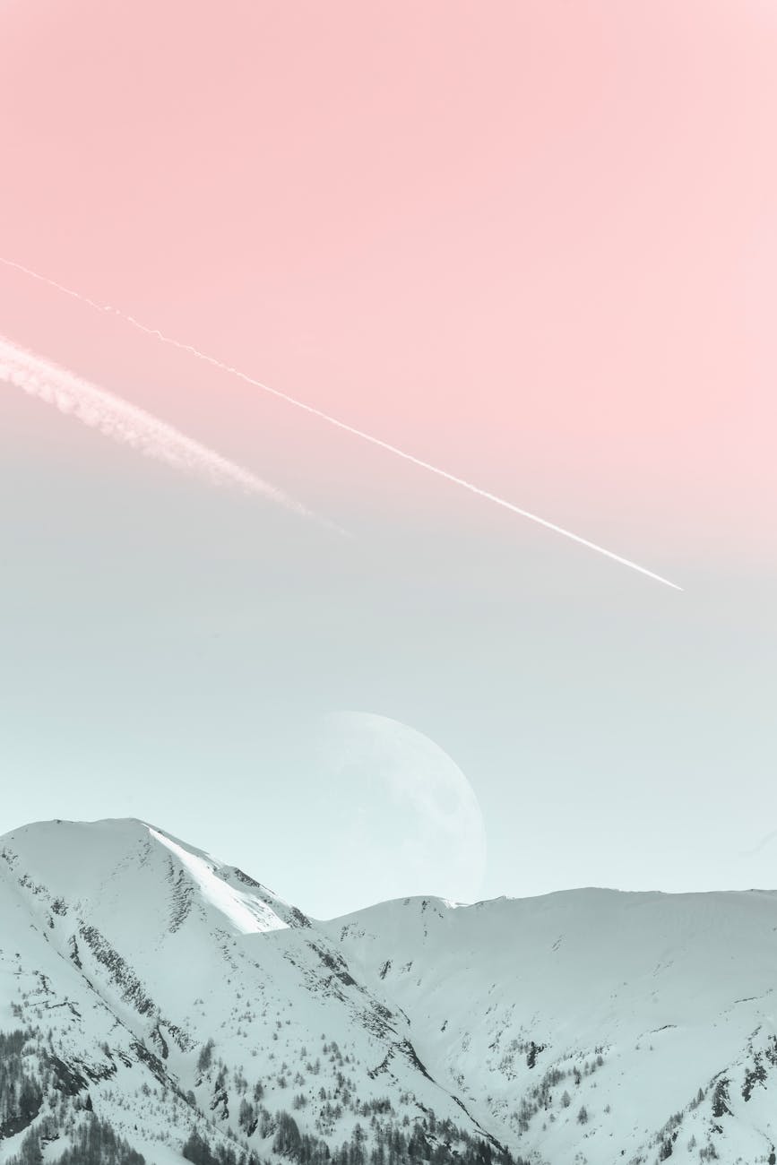 A tranquil winter landscape showcasing snowy mountains with a pastel-colored sky and visible moon.