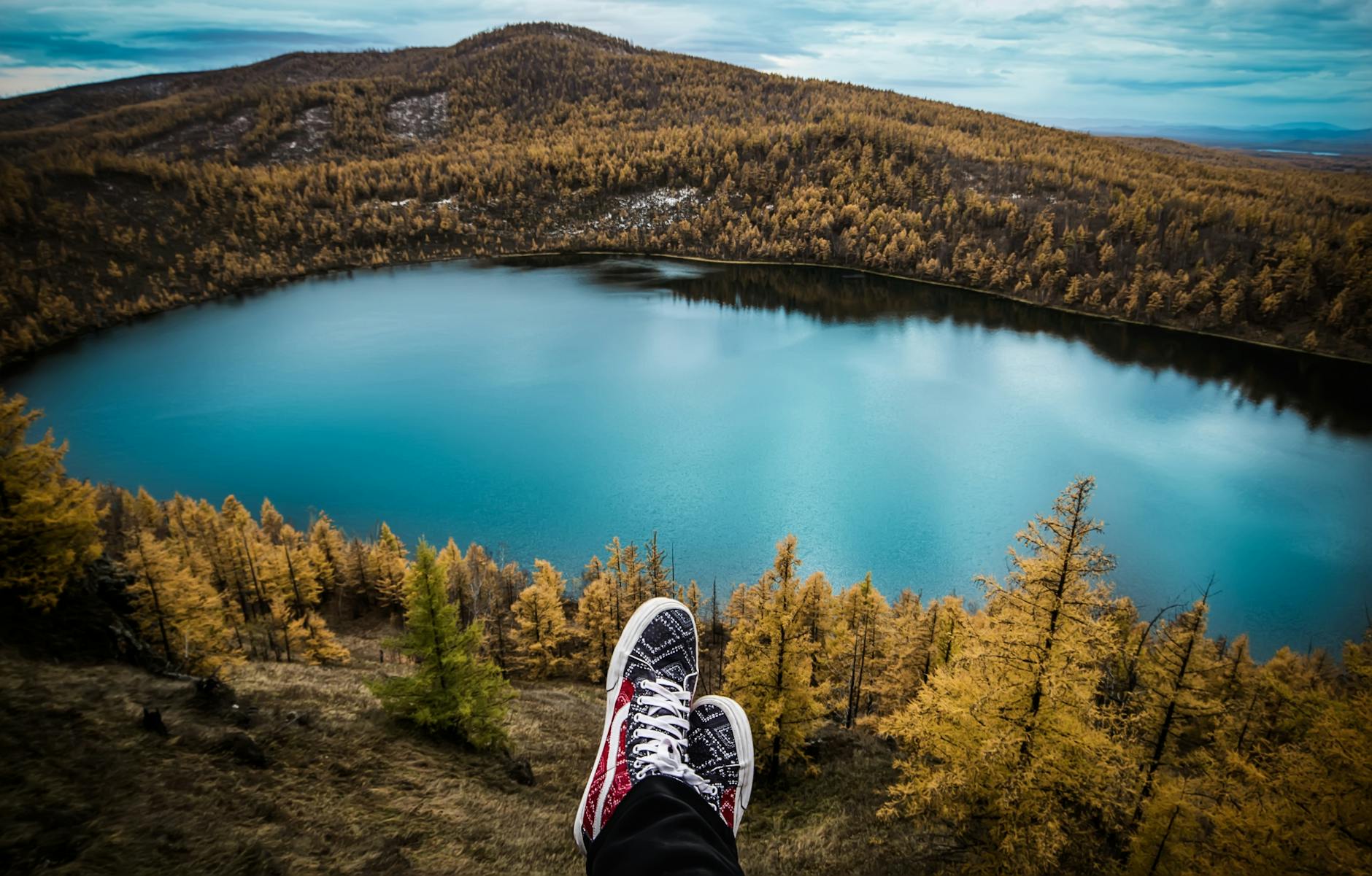 Feet dangle over a scenic mountain lake surrounded by autumn trees, capturing the essence of outdoor adventure. Feet dangle over a scenic mountain lake surrounded by autumn trees, capturing the essence of outdoor adventure.