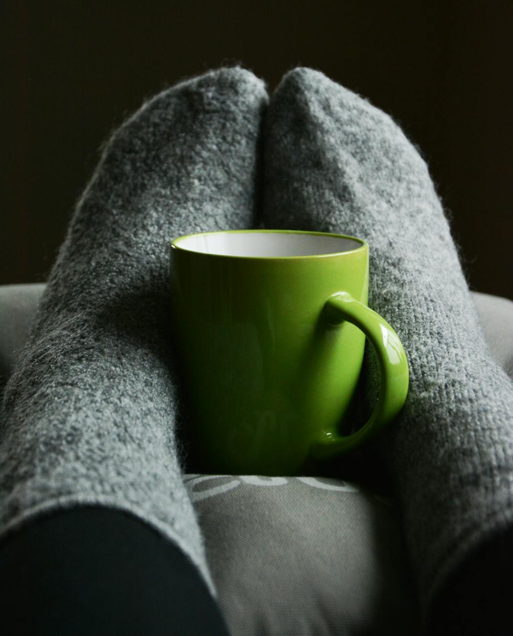Warm and cozy indoor scene with a green mug between gray wool socks, perfect for relaxation.