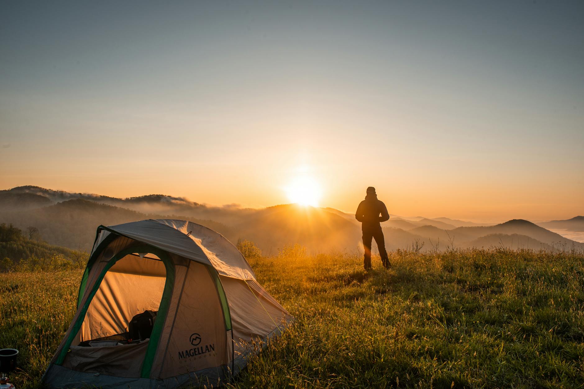 A camper enjoys the sunrise in a mountain setting with a tent. Perfect nature escape.
