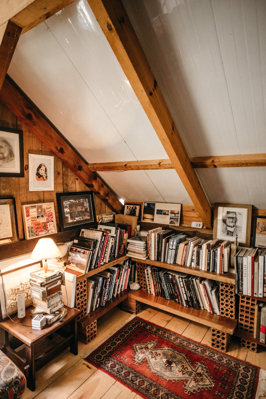 A cozy attic space with wooden bookshelves filled with books and warm lighting.