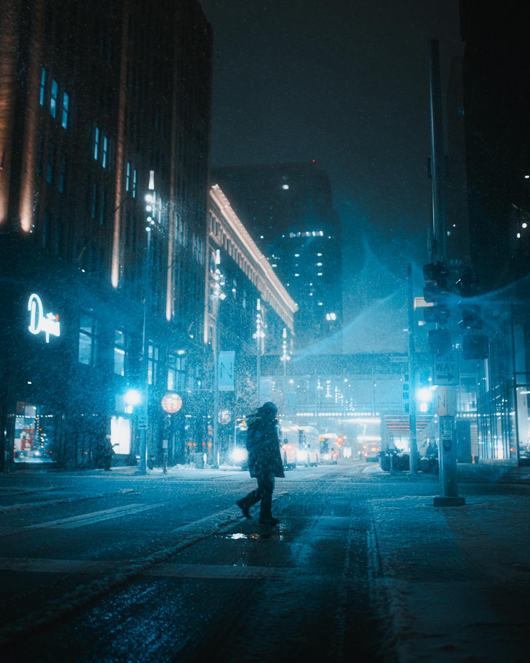 Silhouetted pedestrian crossing a snowy street in downtown Minneapolis at night.