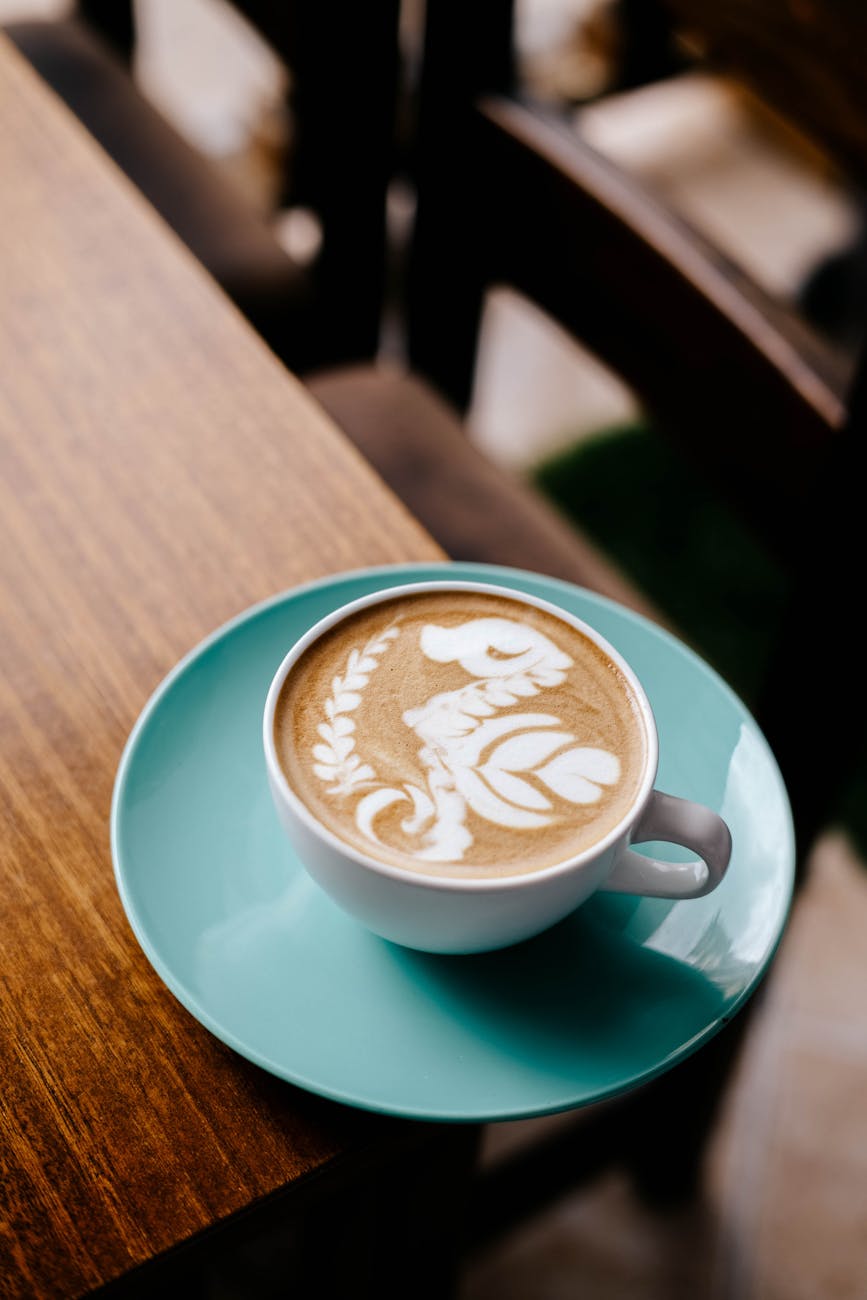 Beautiful coffee latte with intricate latte art served in an aqua cup on a wooden table. Beautiful coffee latte with intricate latte art served in an aqua cup on a wooden table.