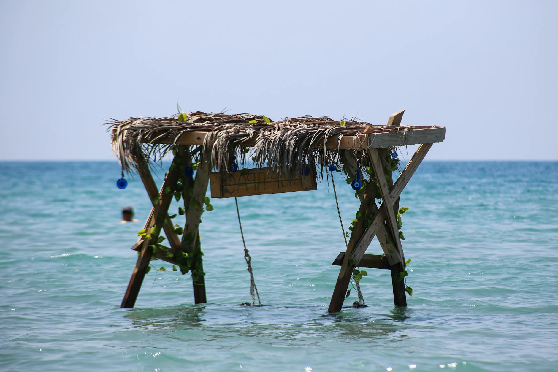 A rustic wooden structure with a thatched roof standing in clear ocean waters under a bright blue sky. A rustic wooden structure with a thatched roof standing in clear ocean waters under a bright blue sky.