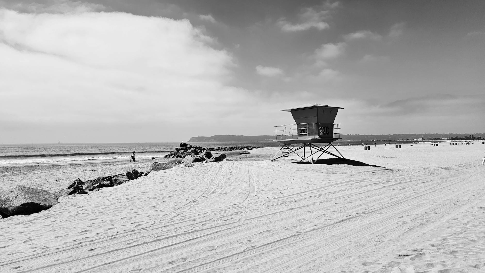 A serene black and white image of a beach with a lifeguard tower and distant walkers. A serene black and white image of a beach with a lifeguard tower and distant walkers.