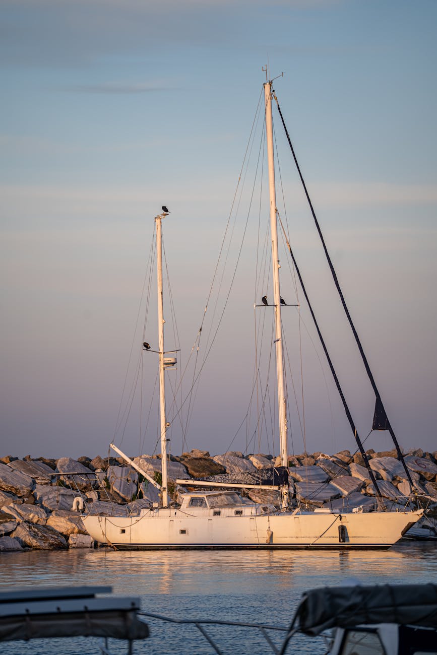 Sailboat docked by a rocky marina at sunset, serene ocean view.