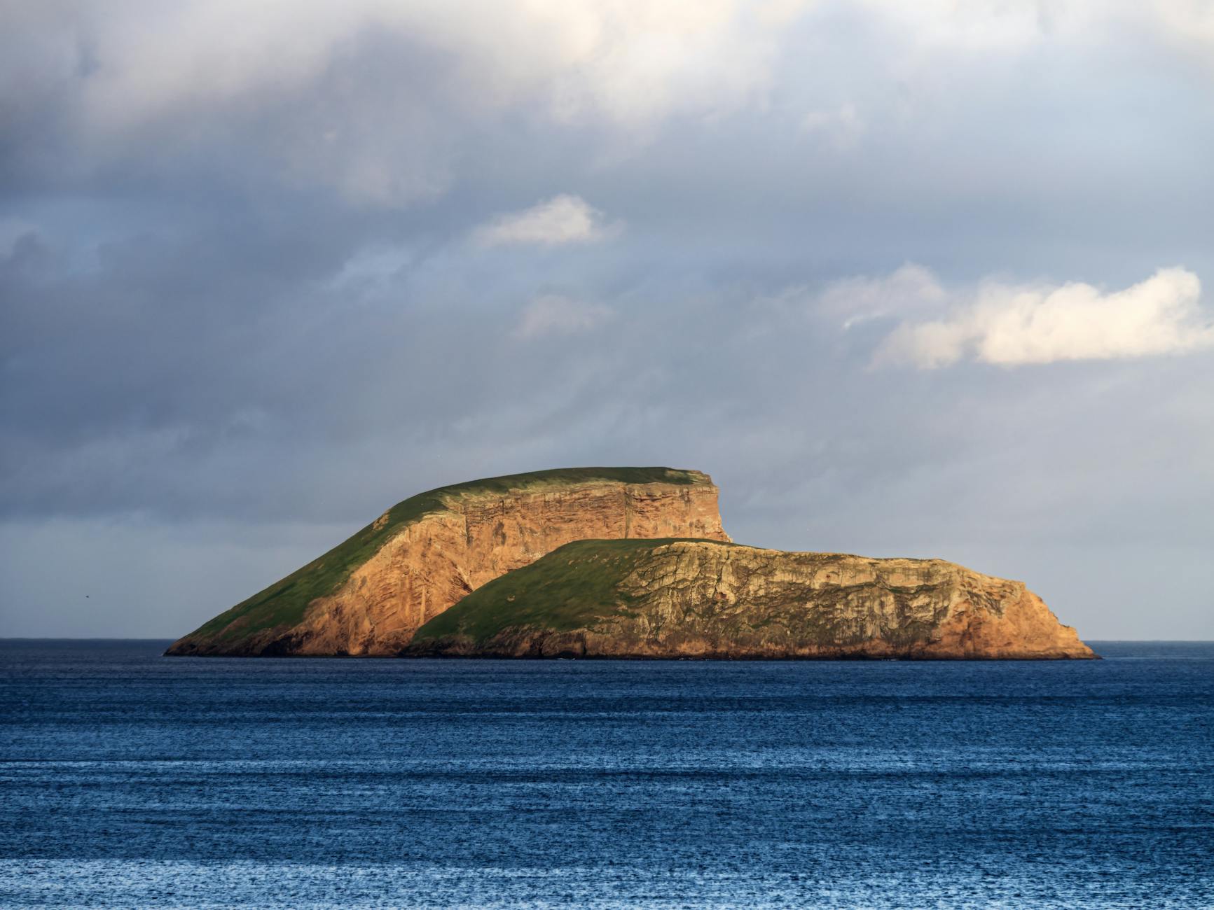 Beautiful view of a small island surrounded by deep blue water and under a cloudy sky.