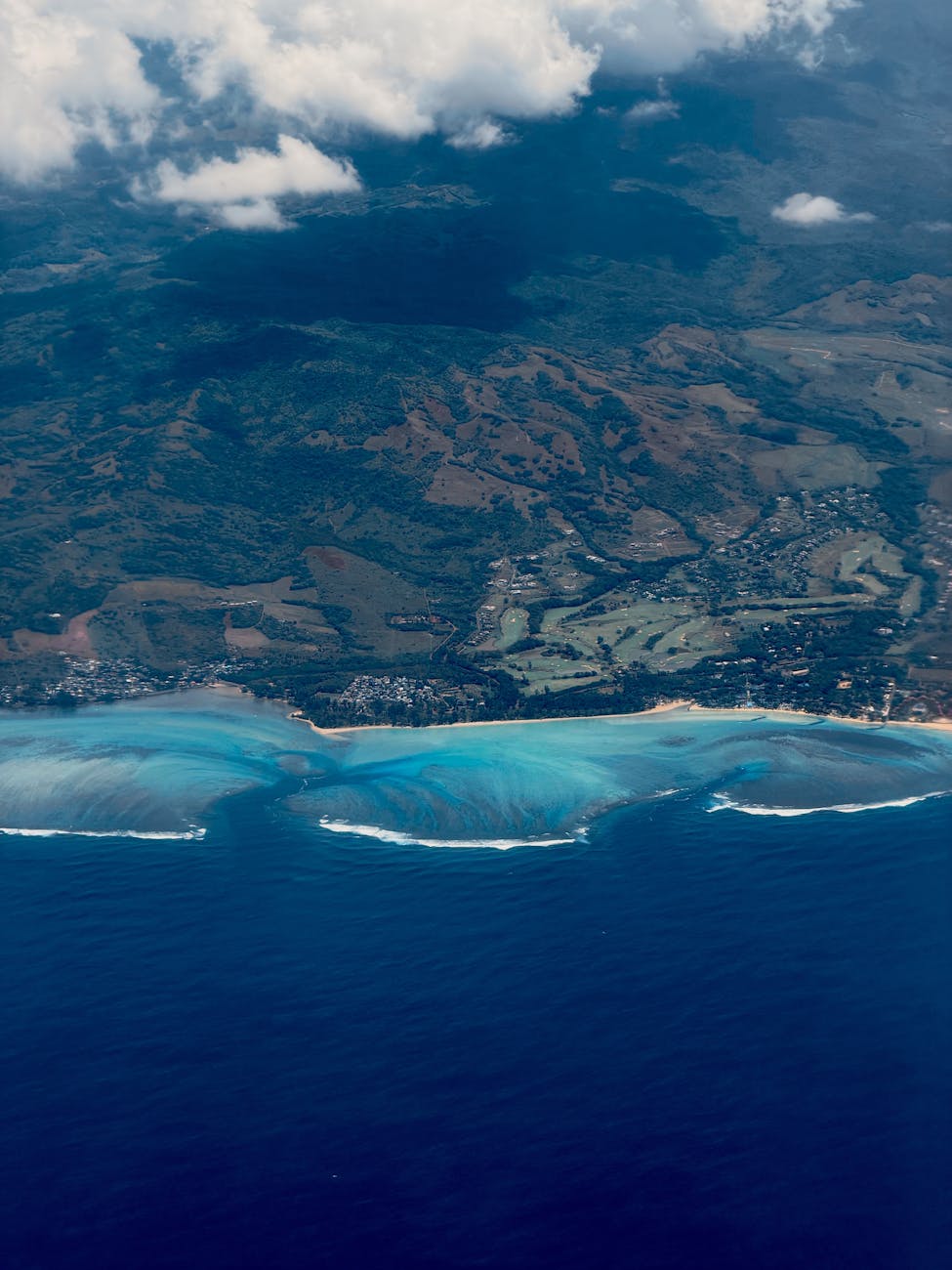 Stunning aerial view of a vibrant coastline and lush landscape beneath scattered clouds.