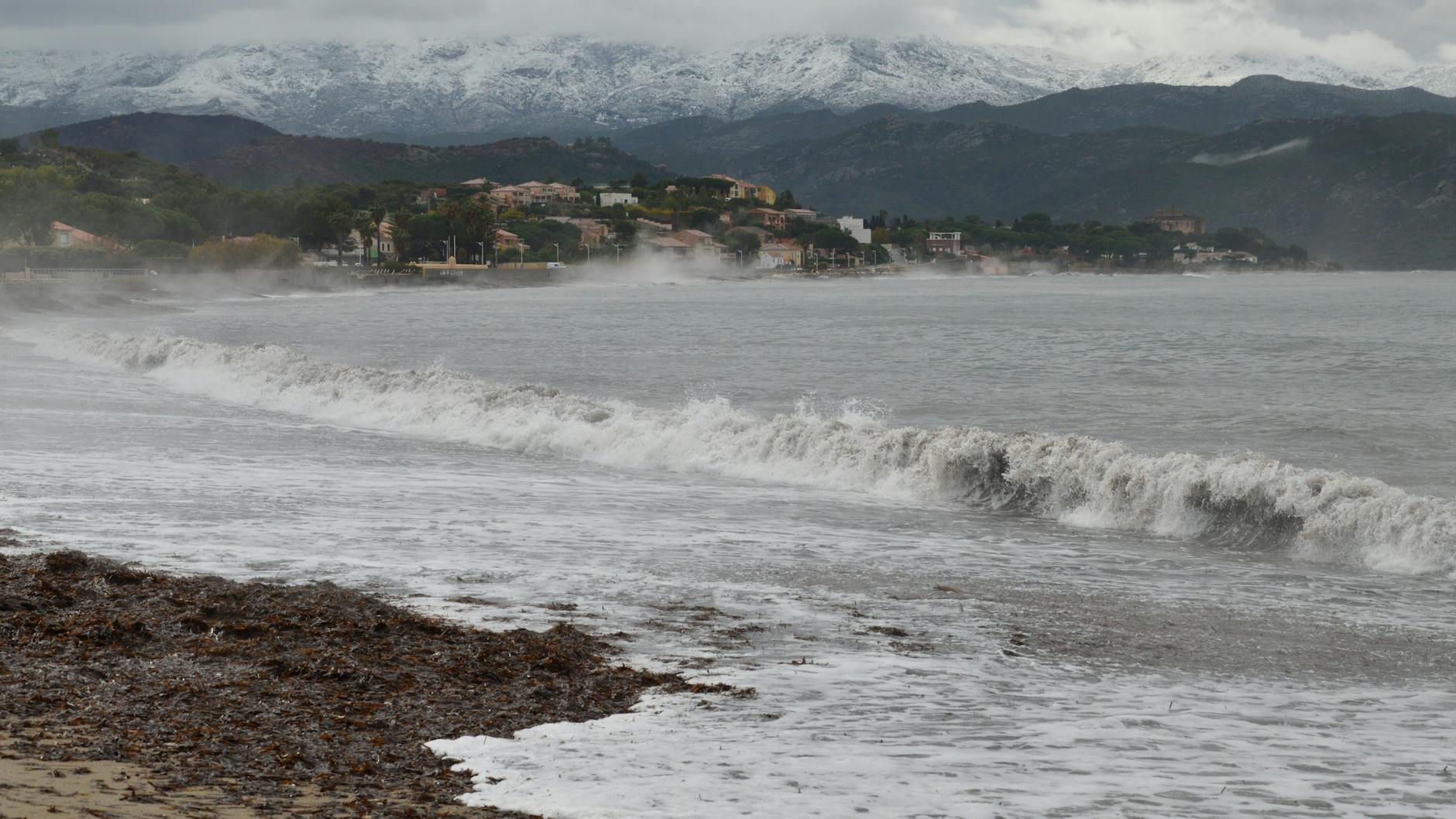 Captivating view of Saint-Florent beach with mist over the sea and snow-capped mountains.