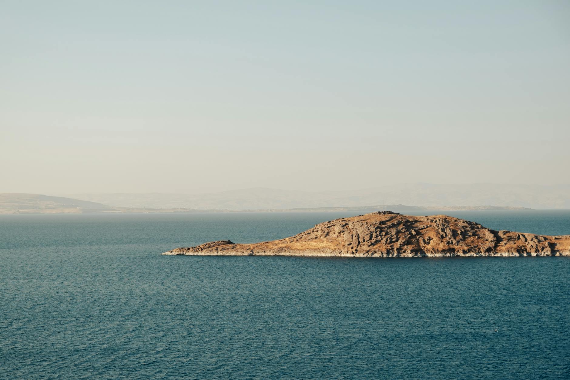 Peaceful distant view of an island surrounded by calm blue sea under clear sky. Peaceful distant view of an island surrounded by calm blue sea under clear sky.